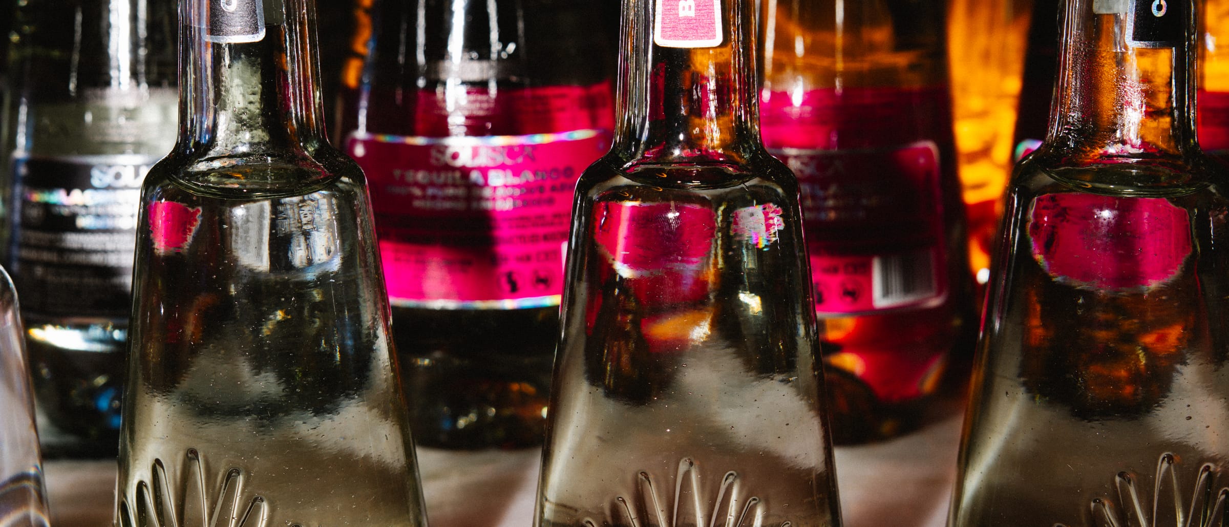 Rows of Solisca tequila bottles with alternating pink and black labels in warm light.