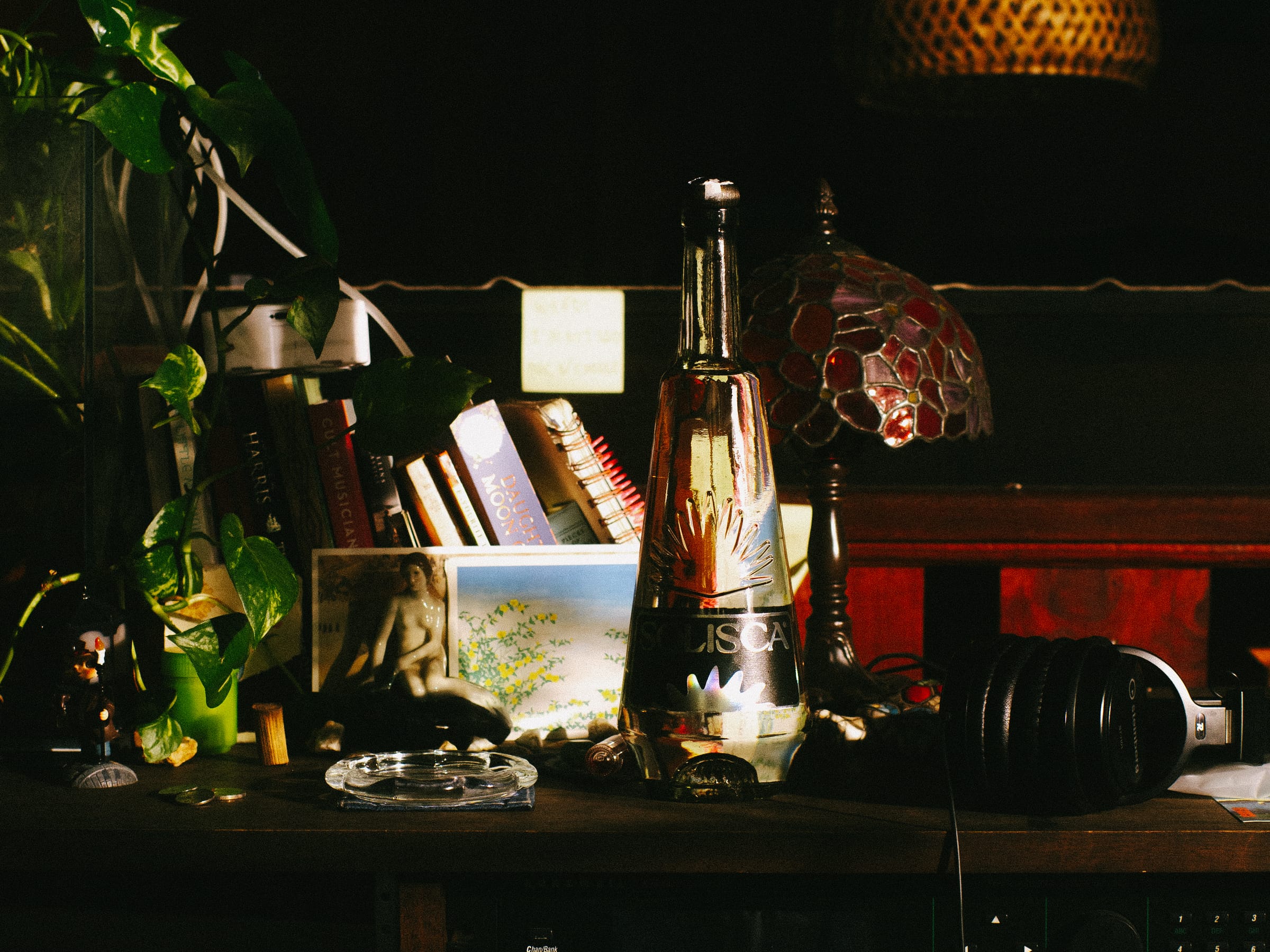 A Solisca bottle on a wooden sideboard beside a lamp, tapes, and music equipment in a warm room.