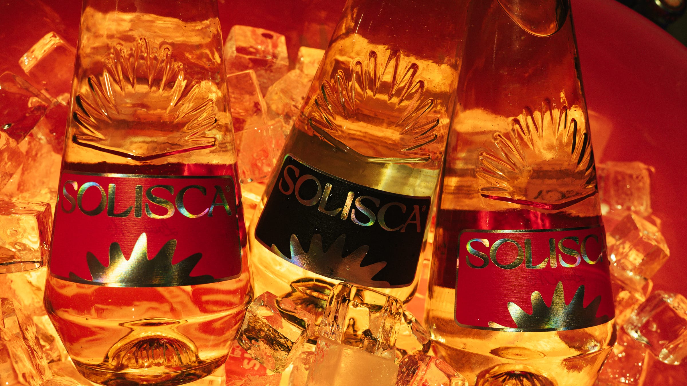 Three Solisca bottles standing in glowing ice inside a red bucket.