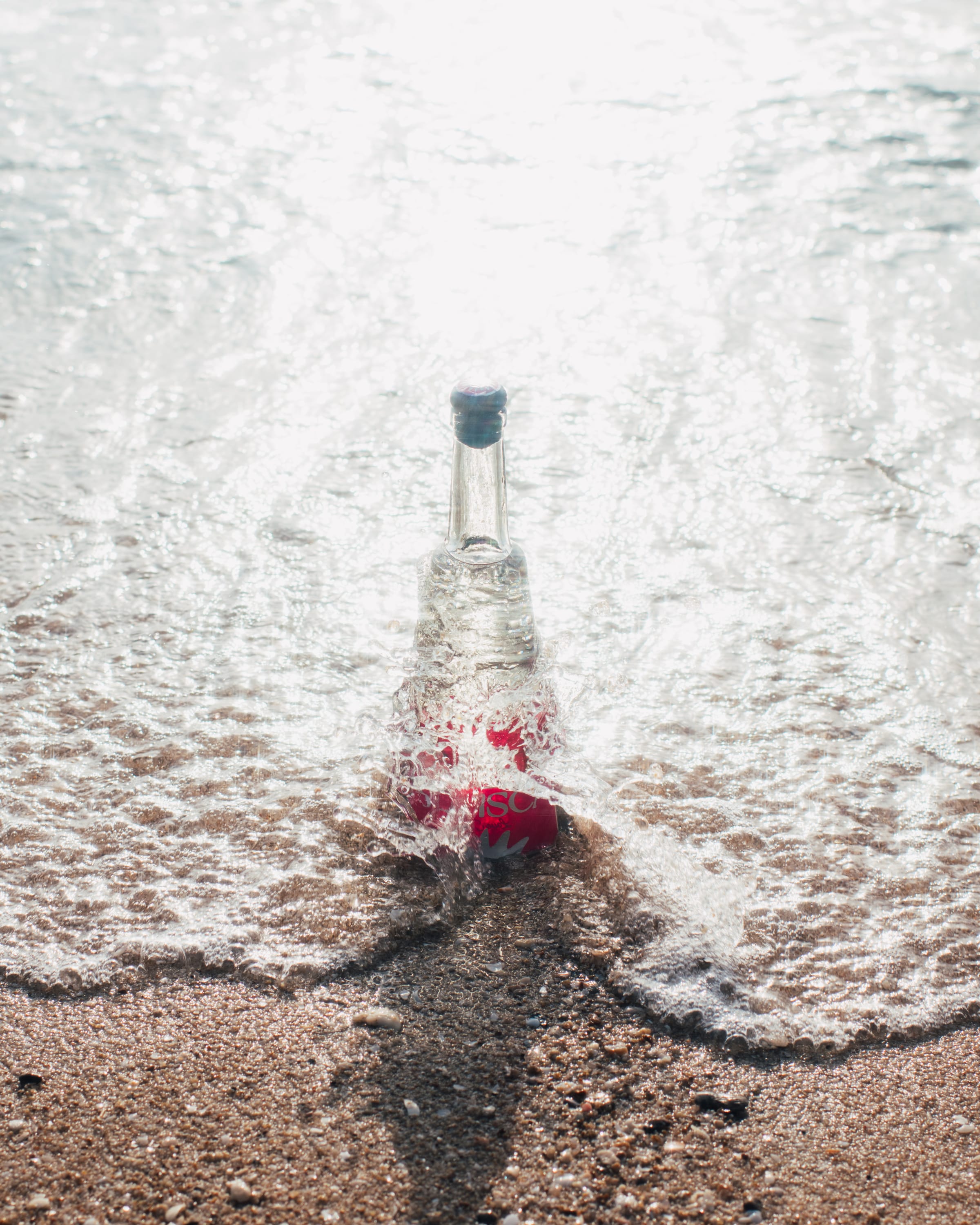 Surf foam wrapping around a standing Solisca Blanco bottle, seen from above.