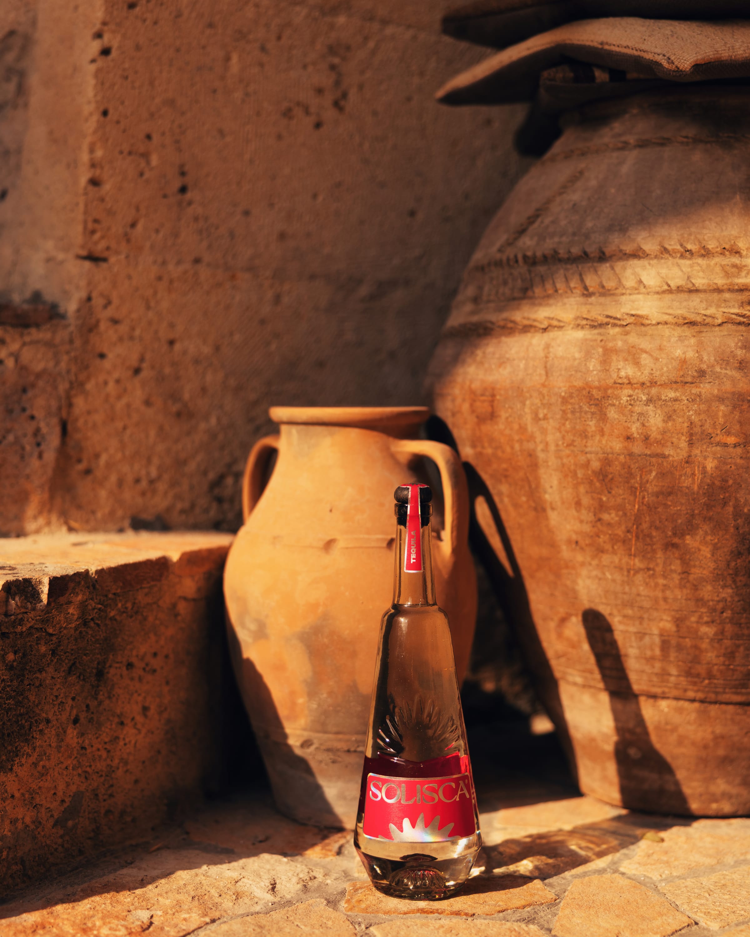 A Solisca Blanco bottle in full golden light beside an amphora against warm stone.