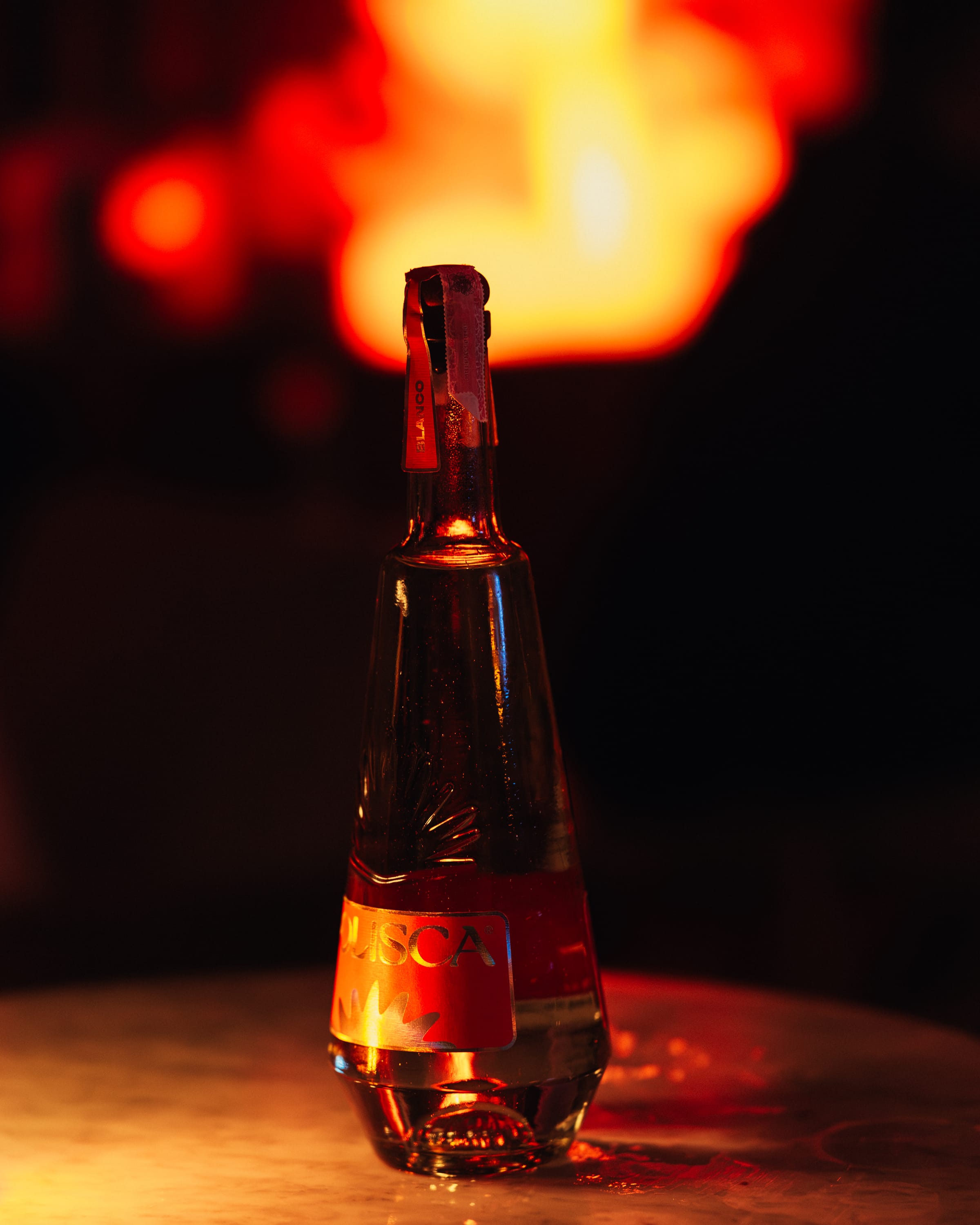 A Solisca Blanco bottle on marble with molten red bokeh light behind it at night.